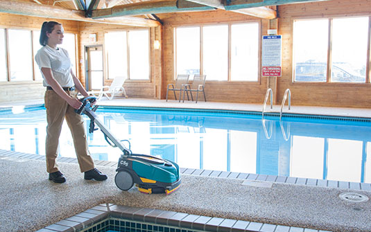 Tennant CS5 walk behind floor scrubber cleaning a residential pool area