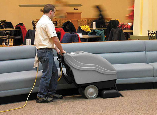 cleaning staff using a Tennant Company walk-behind carpet extractor to clean carpet in school auditorium