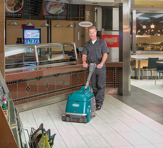 A worker cleans a small format restaurant with a small battery auto scrubber