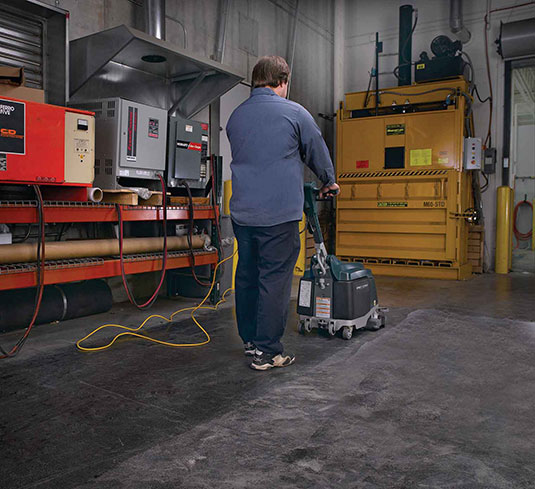 Uma trabalhadora efetua a manutenção de um pavimento de betão polido com uma auto lavadora.